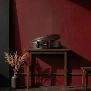 Ceinture homme en cuir grainé marron à boucle métallique posée sur une table en bois